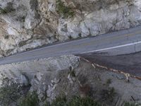 the side of a cliff with cars traveling down it and people walking on a street below