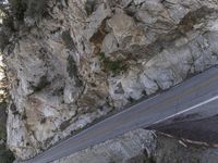 the side of a cliff with cars traveling down it and people walking on a street below