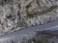 the side of a cliff with cars traveling down it and people walking on a street below