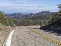 a couple of yellow lines on a road near a mountain area with some trees in the distance