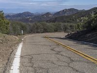 a couple of yellow lines on a road near a mountain area with some trees in the distance