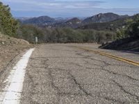 a couple of yellow lines on a road near a mountain area with some trees in the distance