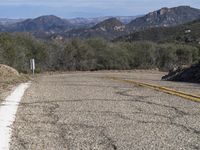 a couple of yellow lines on a road near a mountain area with some trees in the distance