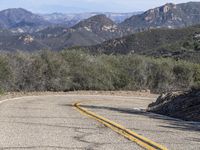 a couple of yellow lines on a road near a mountain area with some trees in the distance