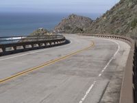 a large paved winding road with two lanes over the ocean's edge, with two cars driving along it