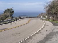 a large paved winding road with two lanes over the ocean's edge, with two cars driving along it