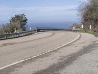 a large paved winding road with two lanes over the ocean's edge, with two cars driving along it