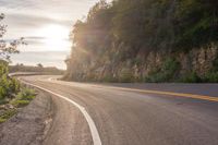 the sun is shining on an empty mountain road as it passes by a stone cliff face