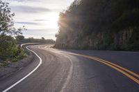 the sun is shining on an empty mountain road as it passes by a stone cliff face