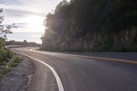 the sun is shining on an empty mountain road as it passes by a stone cliff face