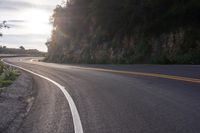 the sun is shining on an empty mountain road as it passes by a stone cliff face