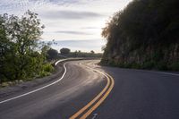 the sun is shining on an empty mountain road as it passes by a stone cliff face