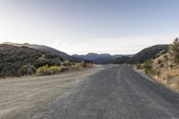 an empty dirt road winding through the mountains with no traffic on it in front of a gated off sign