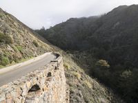 a person is riding a motorcycle down a mountain road next to a cliff side near the ocean