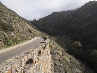 a person is riding a motorcycle down a mountain road next to a cliff side near the ocean