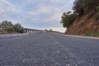 a motorcycle driving down a winding road under an overcast sky with some clouds in the distance