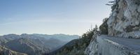 the view from a road overlooks mountains and pine trees as it is partly cloudy