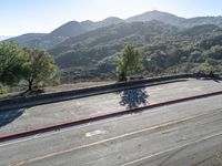 a road surrounded by mountains covered with trees and green bushes the street ends in red curbing and a man riding on a motor cycle