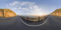 a panoramic view looking down a mountain road from a vantage with a wooden fence in the middle