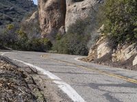 a man riding a bike down the road on a mountain road with rocks and trees behind