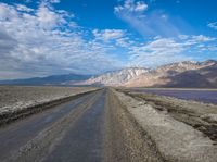 dirt road with mountains in background under blue sky and clouds over water with dirt road in foreground