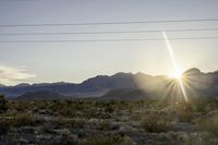 a sun setting on a desert with mountains in the distance and electrical poles hanging above