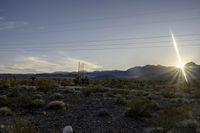 a sun setting on a desert with mountains in the distance and electrical poles hanging above