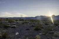 a sun setting on a desert with mountains in the distance and electrical poles hanging above