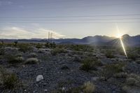 a sun setting on a desert with mountains in the distance and electrical poles hanging above