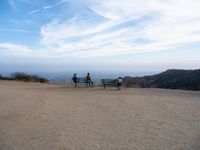 people sitting on a bench on top of a hill watching the ocean from a cliff