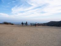 people sitting on a bench on top of a hill watching the ocean from a cliff