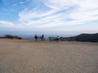 people sitting on a bench on top of a hill watching the ocean from a cliff