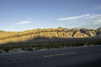 a mountain view from the road as seen in the sunset with a car driving on it