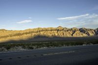 a mountain view from the road as seen in the sunset with a car driving on it