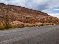 a man riding his motorcycle down the road through mountains with no traffic on it while wearing blue jeans