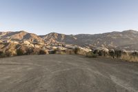 a view of mountains and grass next to dirt road in front of a hill range