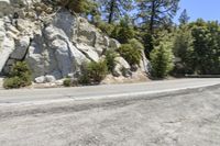 a motorcycle riding down a road next to some rocks and trees in the mountains of california