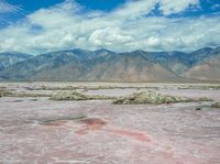 there are many mountains in the distance with some clouds in the sky above them while water is pink and purple