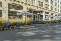 some tables and chairs sit in front of a building with an umbrella on one side