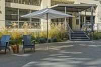 some tables and chairs sit in front of a building with an umbrella on one side