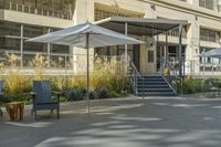 some tables and chairs sit in front of a building with an umbrella on one side