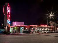 a fast food restaurant lit up at night on a street corner with a clock in the background