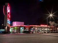 a fast food restaurant lit up at night on a street corner with a clock in the background