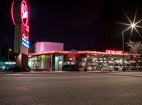 a fast food restaurant lit up at night on a street corner with a clock in the background