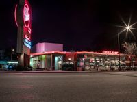 a fast food restaurant lit up at night on a street corner with a clock in the background