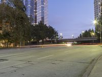 an empty road and some tall buildings with lights at night time outside on a street