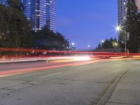 an empty road and some tall buildings with lights at night time outside on a street