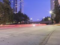 an empty road and some tall buildings with lights at night time outside on a street