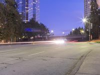 an empty road and some tall buildings with lights at night time outside on a street