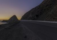 a lone road with a mountain in the background and seagull flying over the ocean